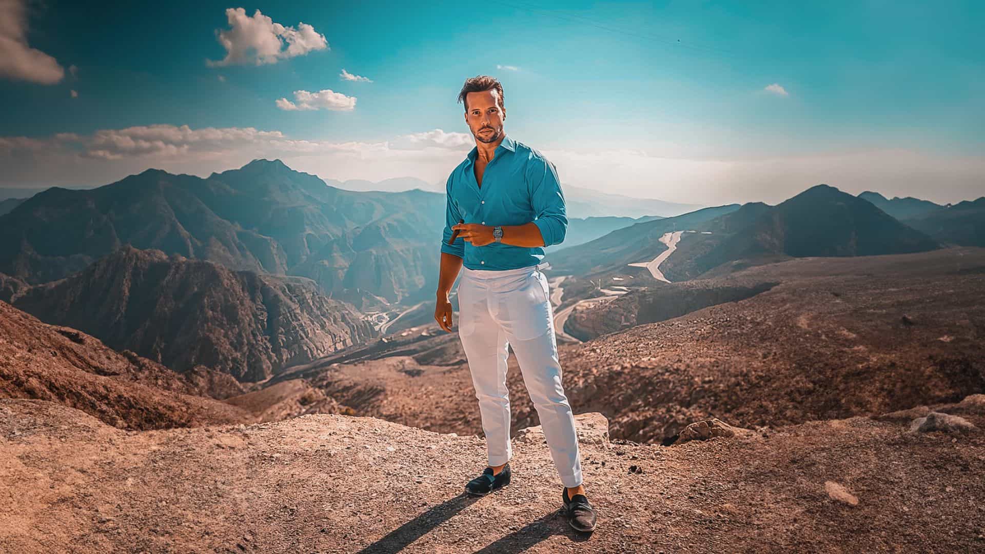 Tristan Tate in a blue shirt standing on top of a mountain